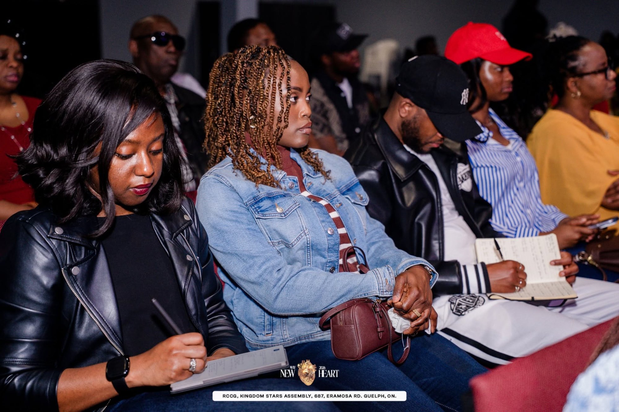 Attendees sit in rows at the New Heart service at Kingdom Stars Assembly, taking notes in notebooks while listening attentively.